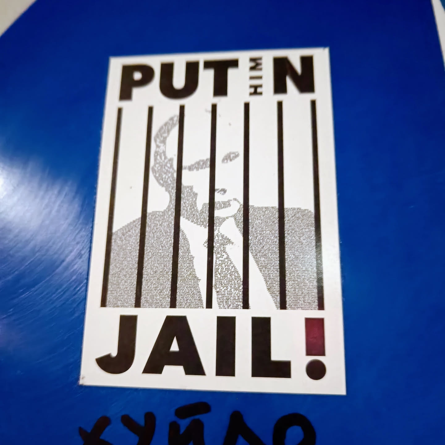 A sticker depicting Vladimir Putin behind bars. The image of Putin is composed of small text.  The sticker has a strong anti-Putin message.