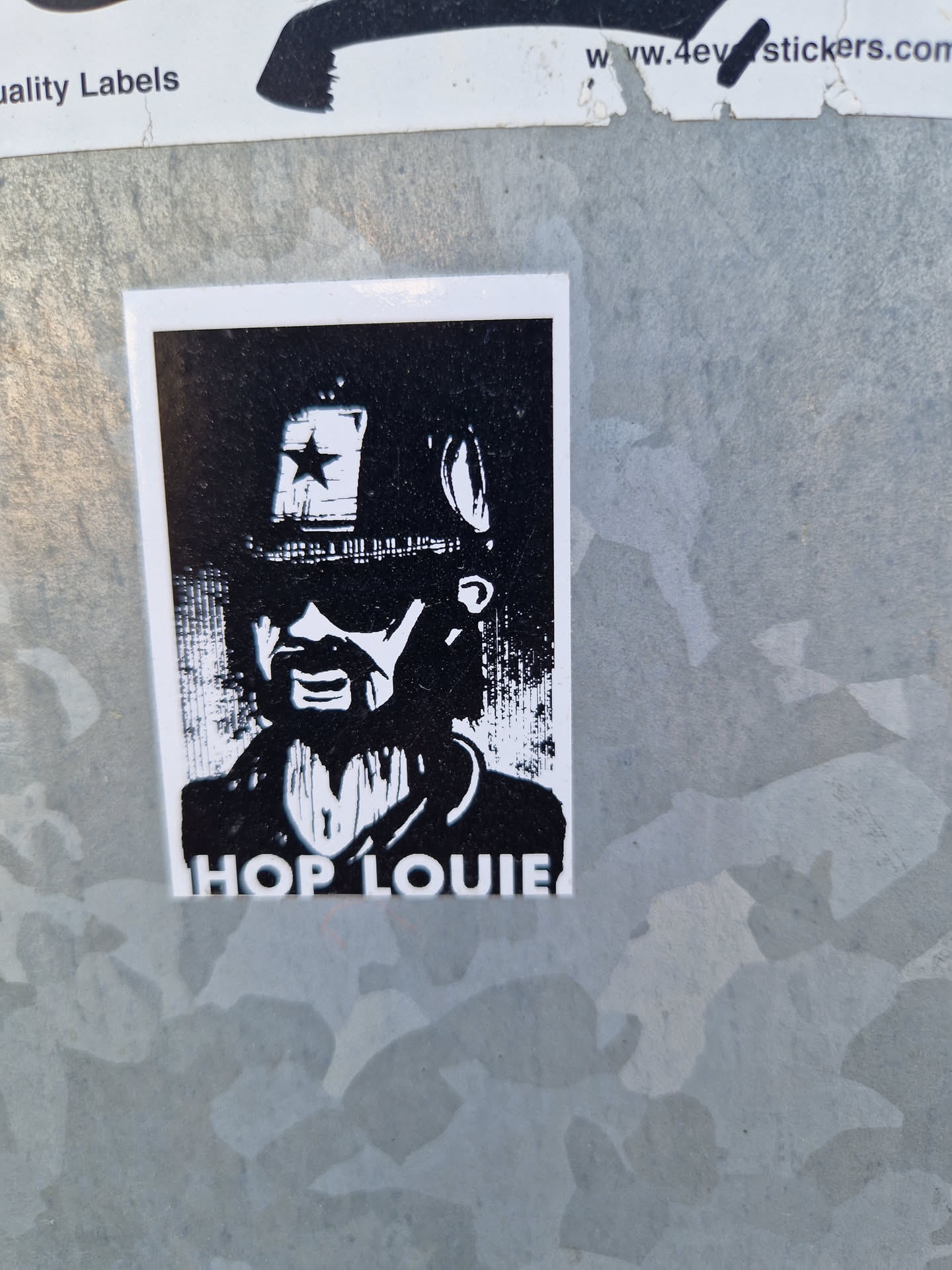 A black and white sticker featuring an illustration of Hop Louie. The sticker has a minimalist design with strong graphic elements. The name "Hop Louie" is printed at the bottom.  The image is a stylized portrait of a person with a hat and sunglasses.