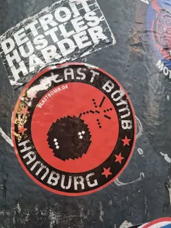 Red and black circular sticker with a pixel art bomb design. It says "Blast Bomb Hamburg" and has a website address blastbomb.de