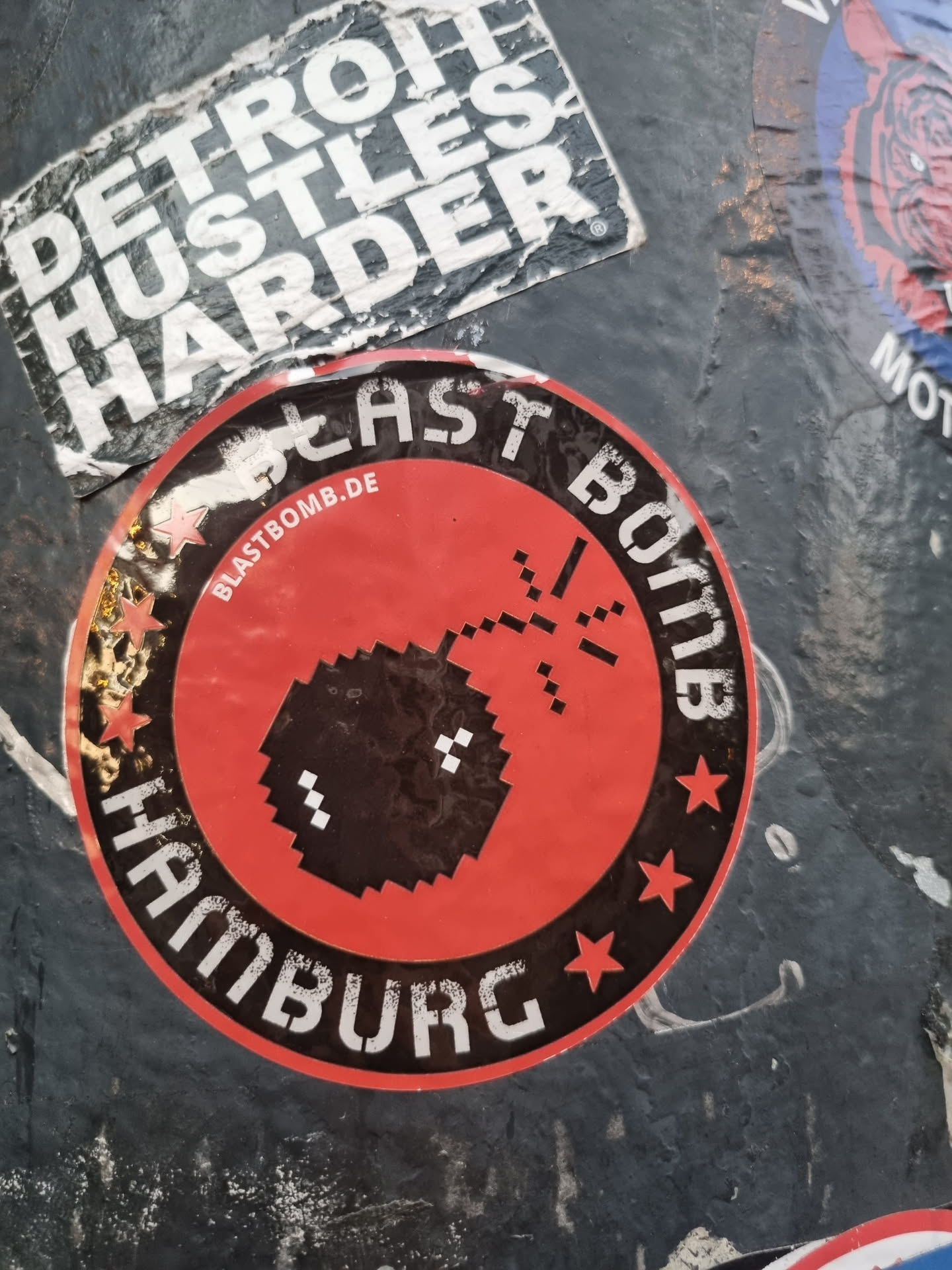 Red and black circular sticker with a pixel art bomb design. It says "Blast Bomb Hamburg" and has a website address blastbomb.de