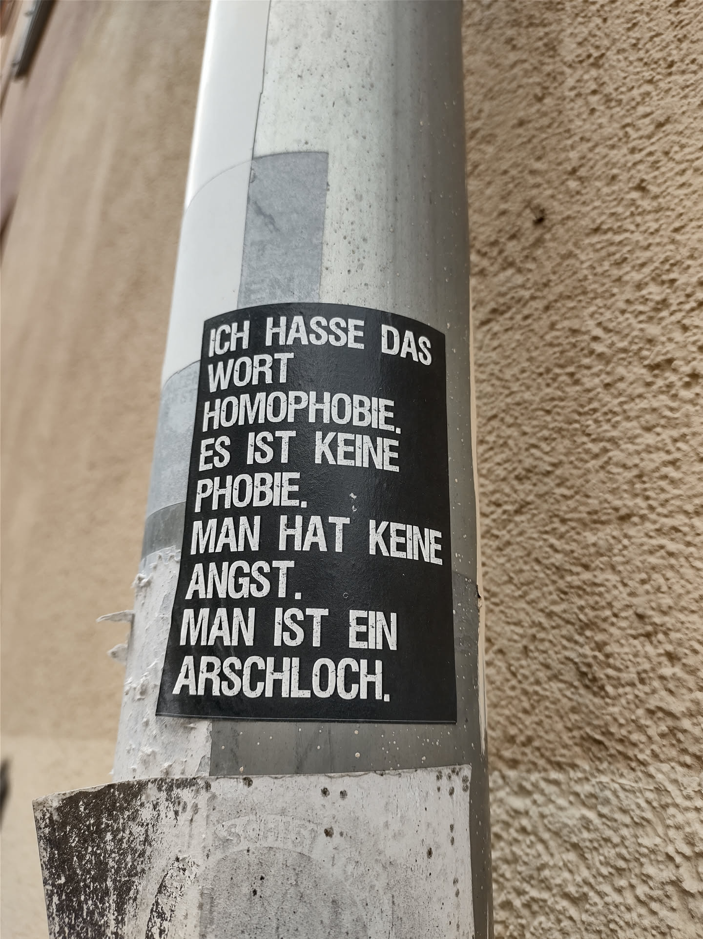 A black and white sticker with a statement against homophobia. The sticker is attached to a pole.