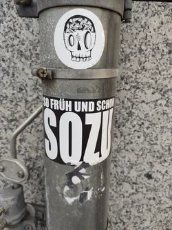 A sticker featuring a skull with its head filled with small objects. Below is another sticker that says SOZU, with the phrase "So früh und schon" written above it.