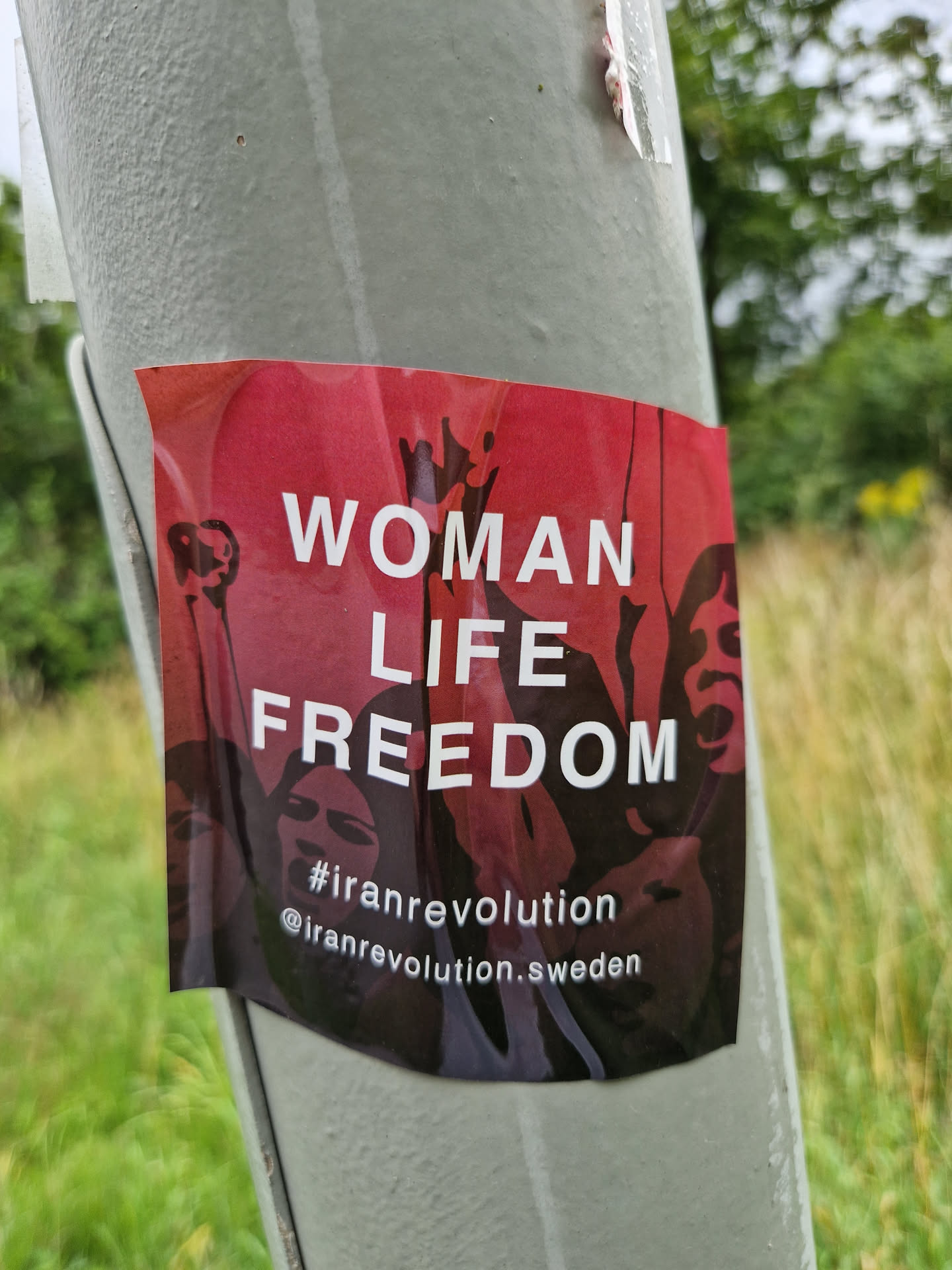 A sticker expressing solidarity with the Iranian Revolution.  It features the slogan "Woman Life Freedom" and includes a social media handle.
