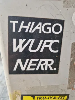 A black and white sticker with the text "THIAGO WUFC NERR." in a sans-serif font. The sticker is affixed to a gray surface.