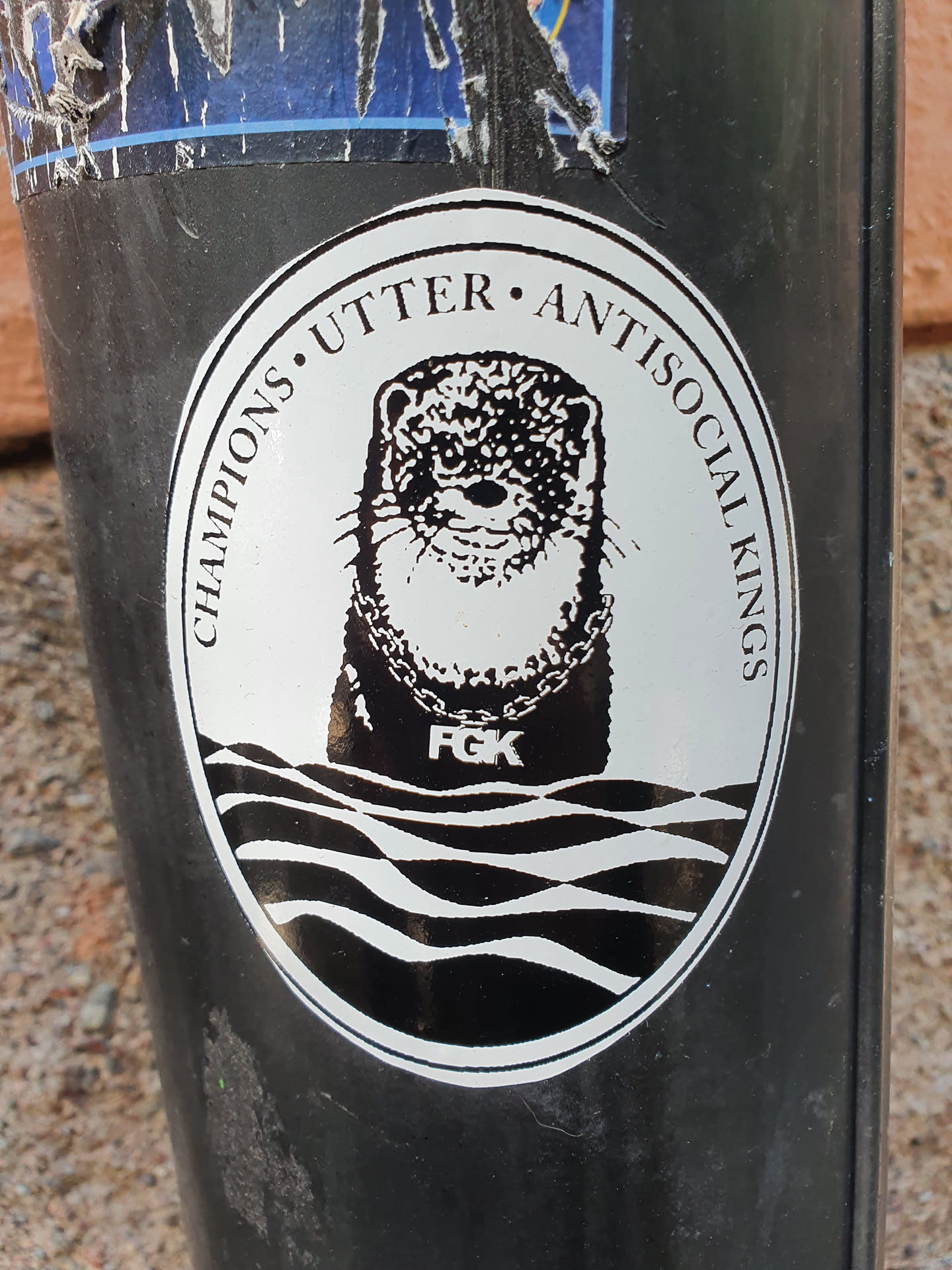 Black and white circular sticker featuring an otter wearing a chain necklace. The text around the otter says "Champions. Utter. Antisocial. Kings."  There are waves at the bottom. The abbreviation "FCK" is visible beneath the otter.