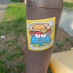 A sticker featuring a cartoon monster character with a hamburger on its head. The character is blue with big eyes and a worried expression. The sticker has a yellow background and some text at the bottom.