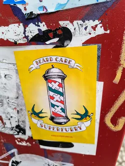Yellow sticker with a barber pole and swallows. The text on the sticker says "Beard Care" and "Superfurry". There is also a website address at the bottom.