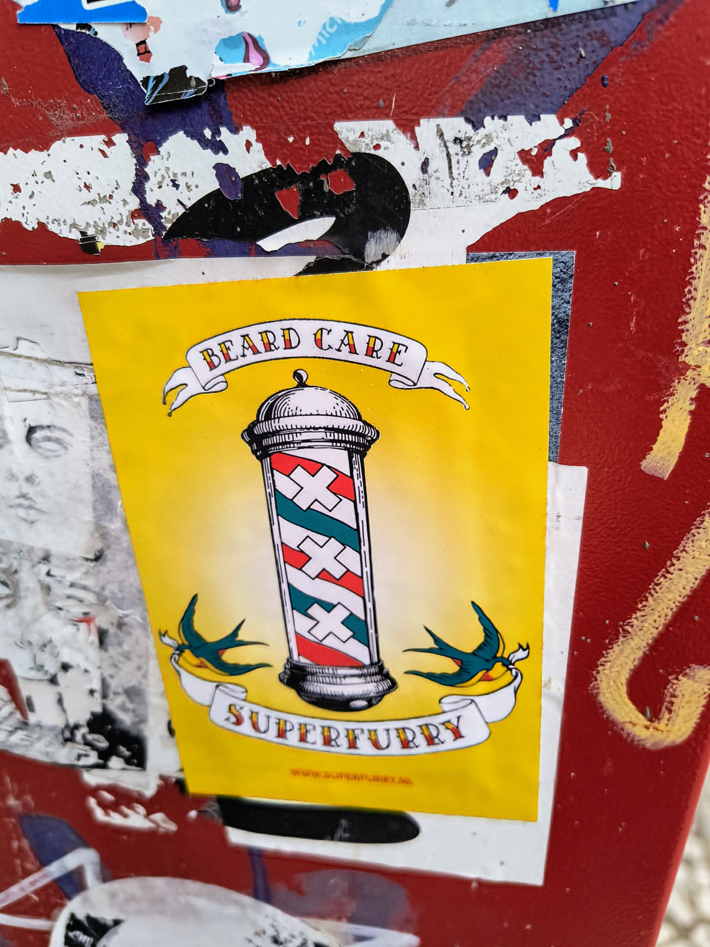 Yellow sticker with a barber pole and swallows. The text on the sticker says "Beard Care" and "Superfurry". There is also a website address at the bottom.