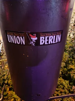 A black sticker with the text "UNION BERLIN" in white.  There is a small graphic of what looks like a soldier or mascot to the left of "UNION" and small text above and below the main text. The small text is partially visible and appears to be in German.
