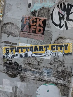 Street sticker A long horizontal sticker with a bold yellow background and checkered yellow-and-white borders on both ends. Prominently displayed across the middle is the text 'STUTTGART CITY' in a heavy black varsity font with white and black outlines. Beneath the lettering is a black-and-white silhouette skyline of recognizable Stuttgart landmarks, including the Fernsehturm Stuttgart (TV tower), stadium, and a Ferris wheel.