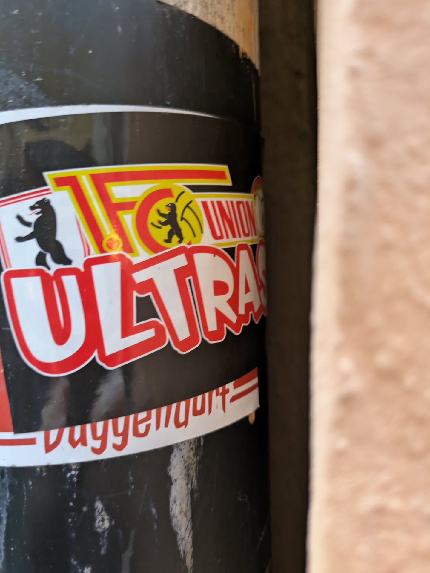 A sticker featuring the logo of the Ultras group of the German football club FC Union Berlin. The sticker is black with red and yellow text and logos. The text "Ultras" is prominently displayed in large red letters, with "FC Union" in smaller yellow letters above it. The logo features two bears and a football. At the bottom, the text "Daygemoult" is visible.