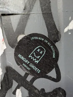 The sticker is round and black with the text "LISTEN NOW ON ALL PLATFORMS" around the edge. It features a teal ghost illustration with "XX" eyes and a wavy mouth. The text "HUNGRY GHOSTS" is printed below the ghost, with "PODCAST" underneath.