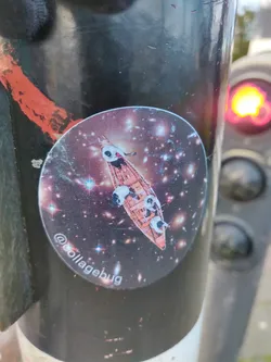 A round sticker featuring an illustration of pandas in a boat traversing a cosmic space filled with galaxies and stars. The sticker has a dark background with sparkling elements, creating a visually captivating scene.