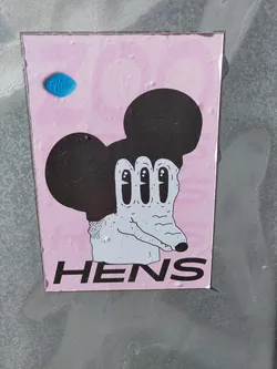 Pink sticker with a drawing of Mickey Mouse's head and a creepy hand with long fingers. The word HENS is written at the bottom of the sticker.