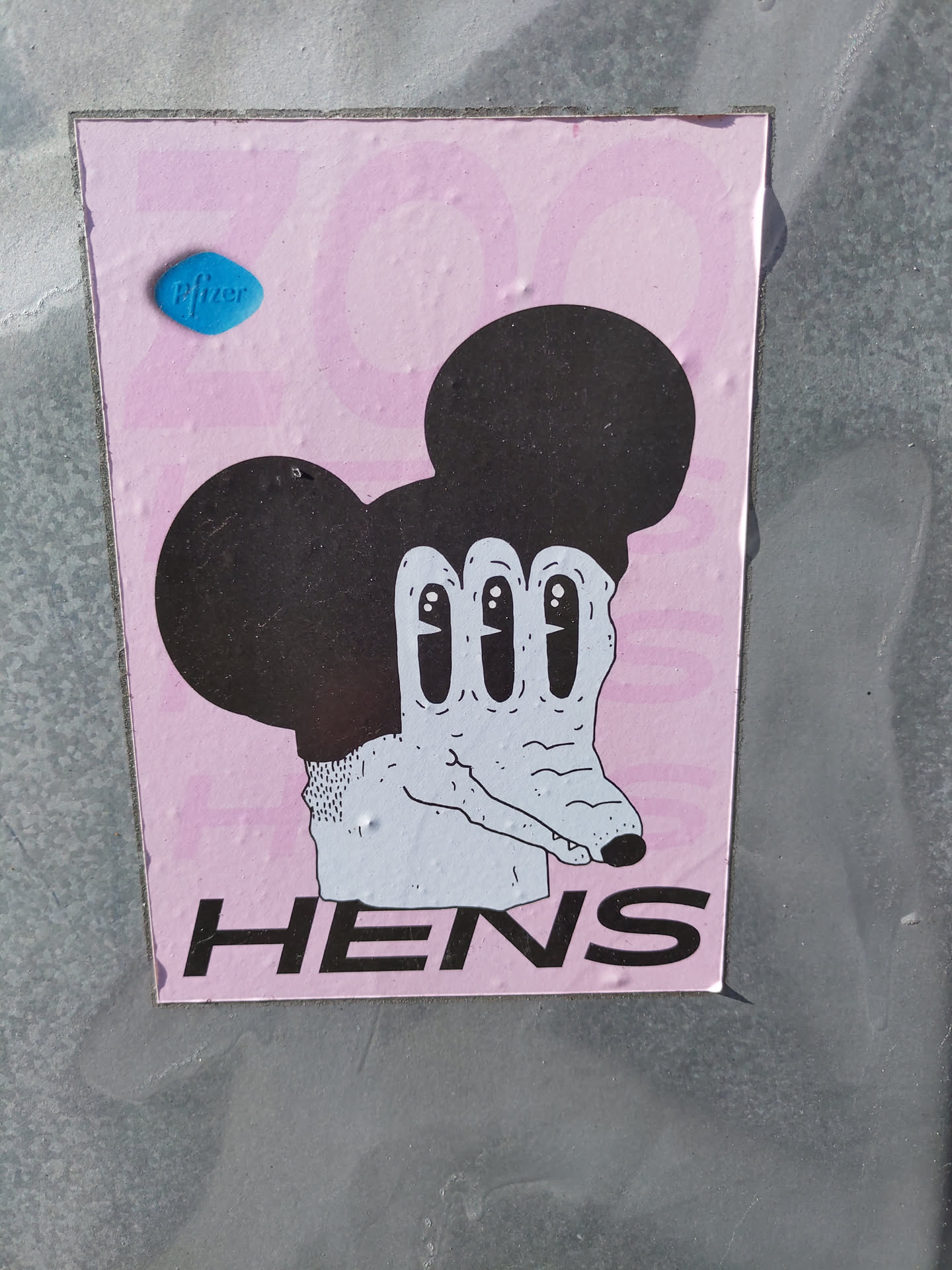 Pink sticker with a drawing of Mickey Mouse's head and a creepy hand with long fingers. The word HENS is written at the bottom of the sticker.