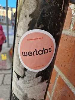 Round pink werlabs sticker on a pole. It says "I samarbete med" (in collaboration with) werlabs.se at the bottom. 