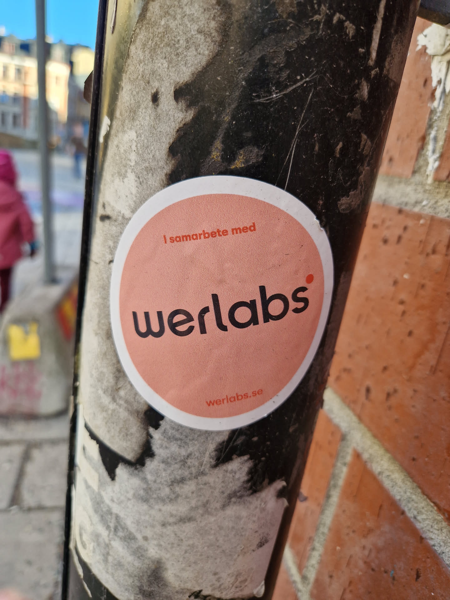 Round pink werlabs sticker on a pole. It says "I samarbete med" (in collaboration with) werlabs.se at the bottom. 