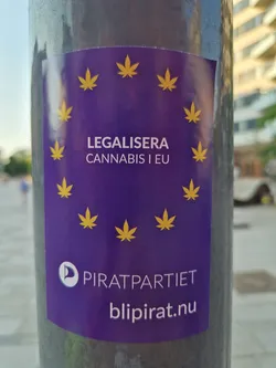 A purple sticker advocating for the legalization of cannabis in the European Union.  It features a stylized EU flag with cannabis leaves and the Pirate Party logo and website.