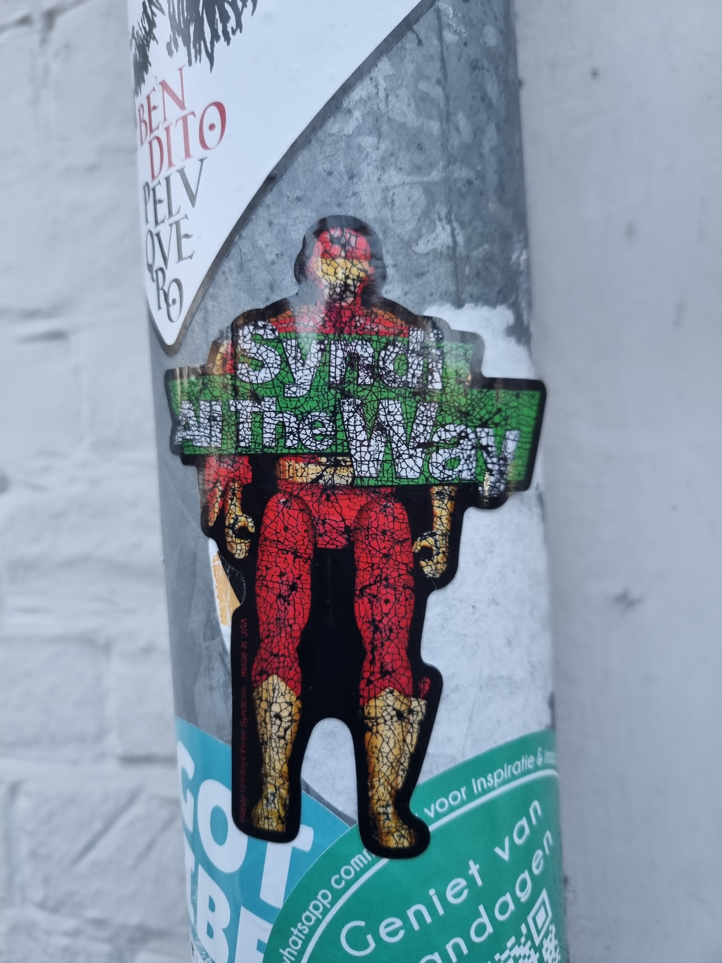This sticker depicts a superhero in a red and gold suit, with the text 'Synth All the Way!' prominently displayed. The style is reminiscent of retro comic books or action figures. The sticker is affixed to a metal pole, alongside other stickers and graffiti. There's a QR code visible on another sticker nearby but not associated with the superhero sticker.