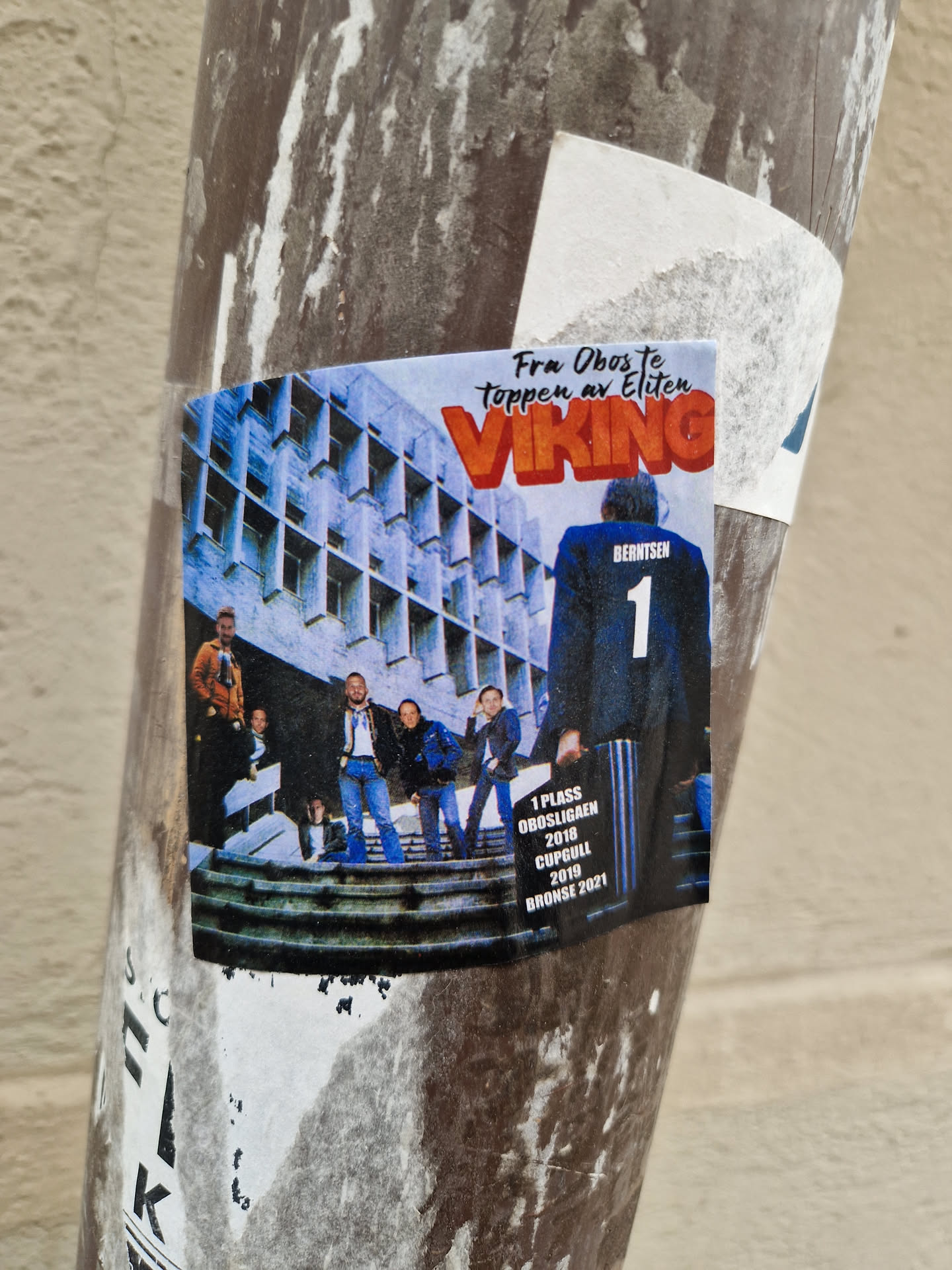 A sticker featuring a photo of a group of people standing on some stairs in front of a building.  The text 'Viking' is prominently displayed, along with information indicating a first-place finish in "Brønnøysund 2018", a cup win in 2019, and a bronze medal in 2021.  The overall aesthetic suggests a sports or team-related theme.