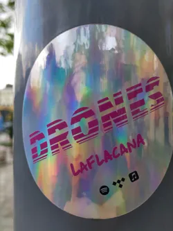Holographic sticker with the text \"DRONES\" and \"LAFLACANA\" in pink. It also contains links to Spotify, Bandcamp and a possible YouTube Music or similar platform.
