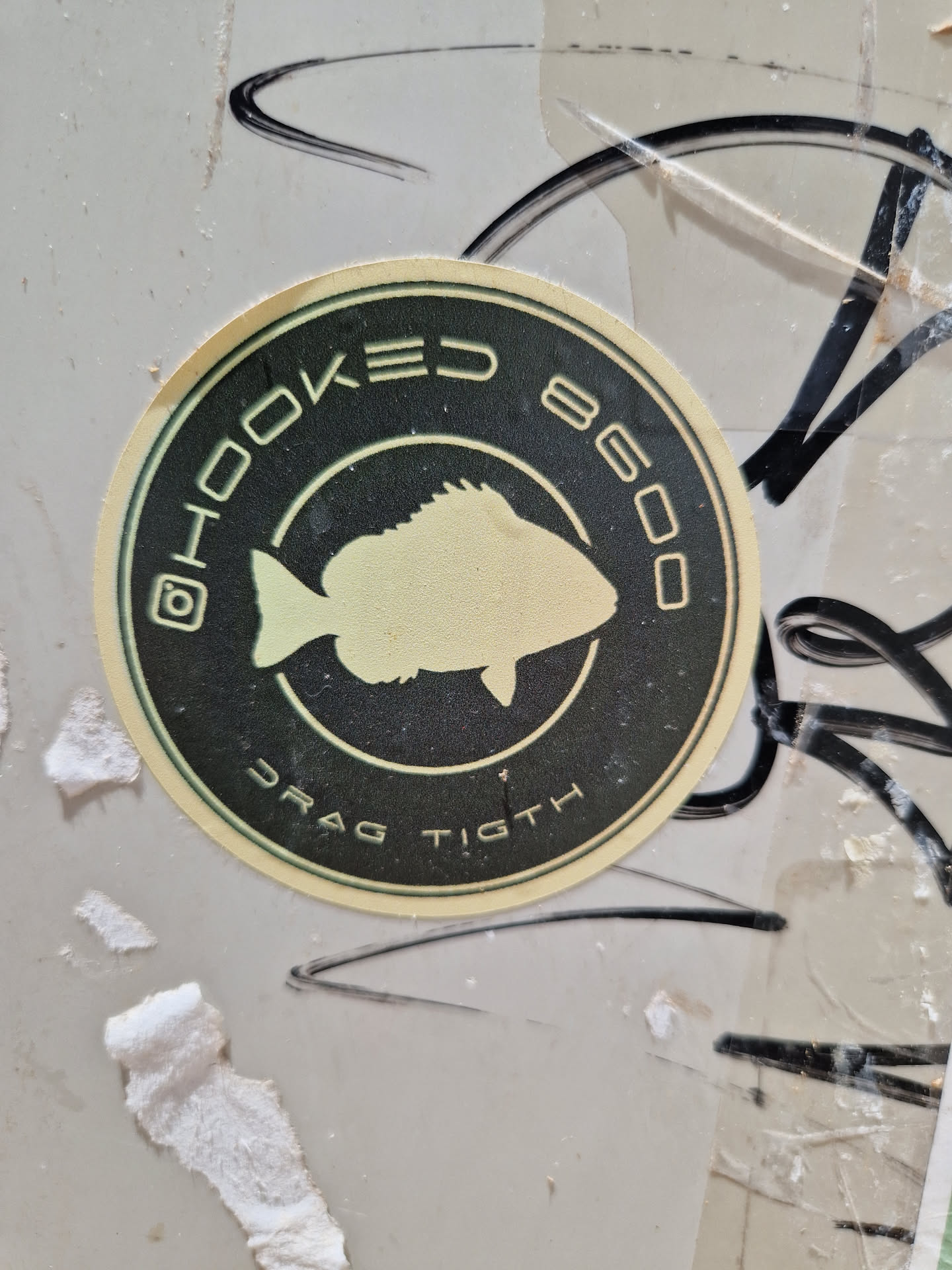 Round sticker with a fish illustration and text. The text includes "HOOKED 8600" and "DRAG TIGHT". There is also an instagram logo.
