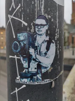 A sticker featuring a man holding a vintage camera. The sticker is mostly blue and white, with a YouTube link at the bottom.