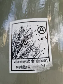 Black and white sticker with an illustration of a bare tree and birds flying away from it.  An anarchy symbol is visible in the upper right corner.  Text at the bottom appears to be in Swedish. The sticker has a slightly worn appearance.