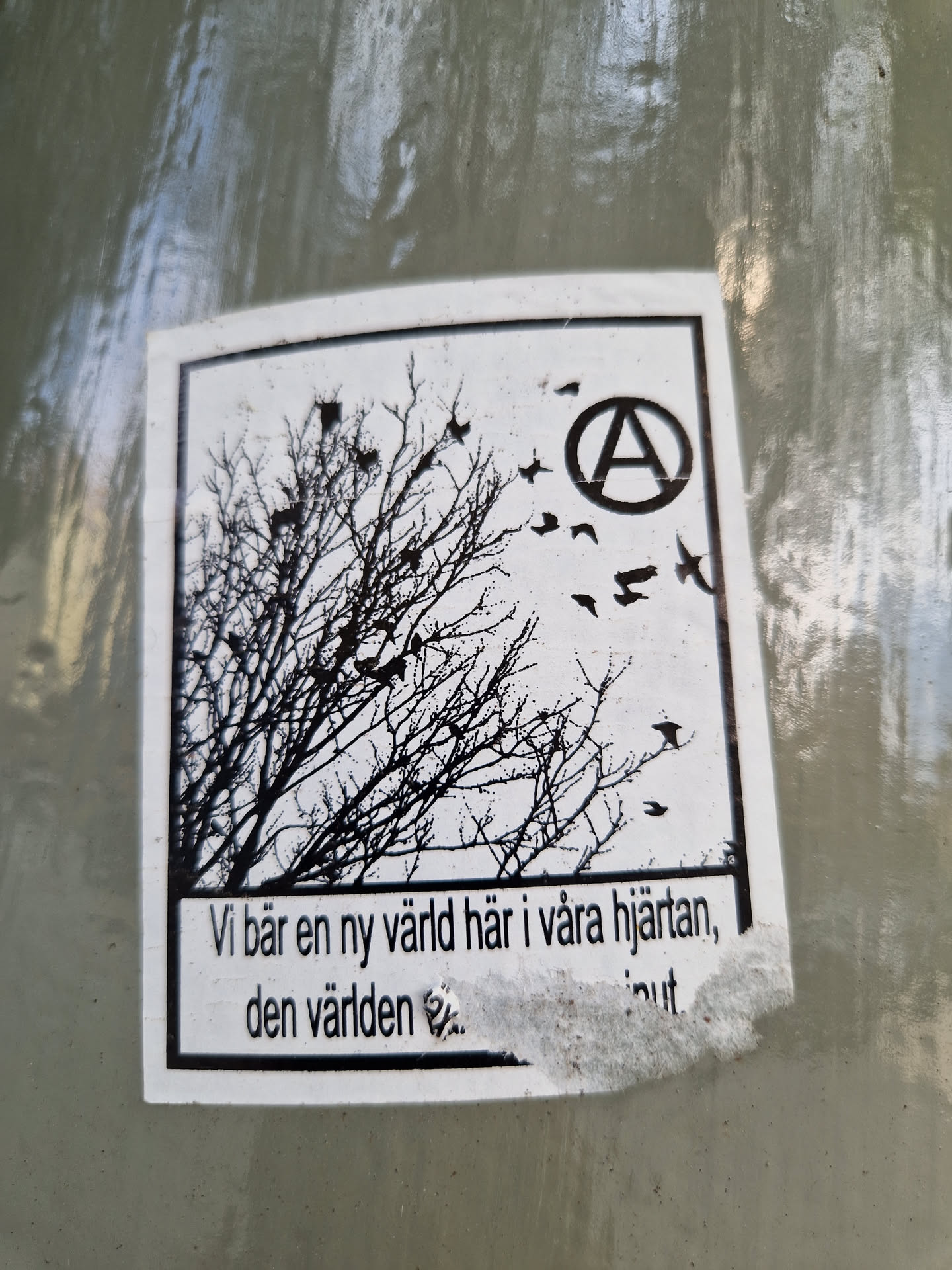 Black and white sticker with an illustration of a bare tree and birds flying away from it.  An anarchy symbol is visible in the upper right corner.  Text at the bottom appears to be in Swedish. The sticker has a slightly worn appearance.