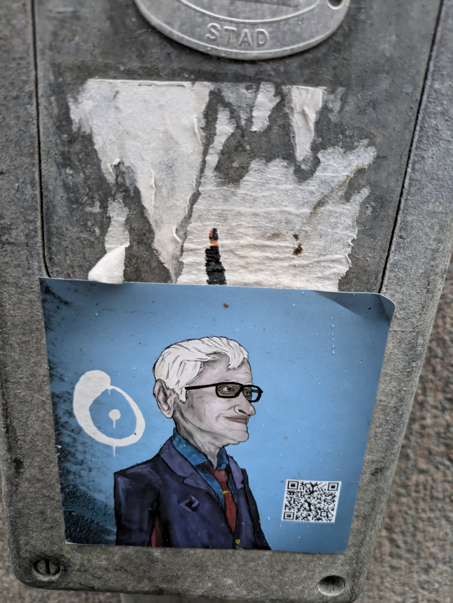 This sticker is an illustration of a man, possibly a portrait, rendered in a somewhat cartoonish style with visible brushstrokes. He is wearing glasses and a suit and tie. The background is a solid light blue.  A QR code is included, potentially linking to more information about the subject or artist.  The sticker itself seems to be hand-drawn and/or digitally printed.
