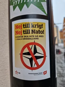 A sticker expressing opposition to war and NATO, featuring a crossed-out NATO compass rose and text in Swedish. The sticker is from the Communist Party of Sweden.