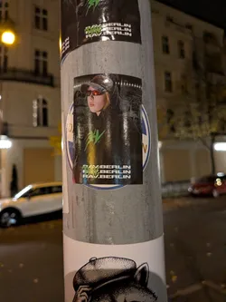 Street sticker A vertical rectangular sticker depicting a person wearing a cap, reflective wraparound sunglasses, and a black hoodie featuring a neon green spiky graphic on the chest. Across the bottom of the sticker, the text 'RAV.BERLIN' is printed three times in bold white uppercase font, overlaid on the left by the same green emblem.