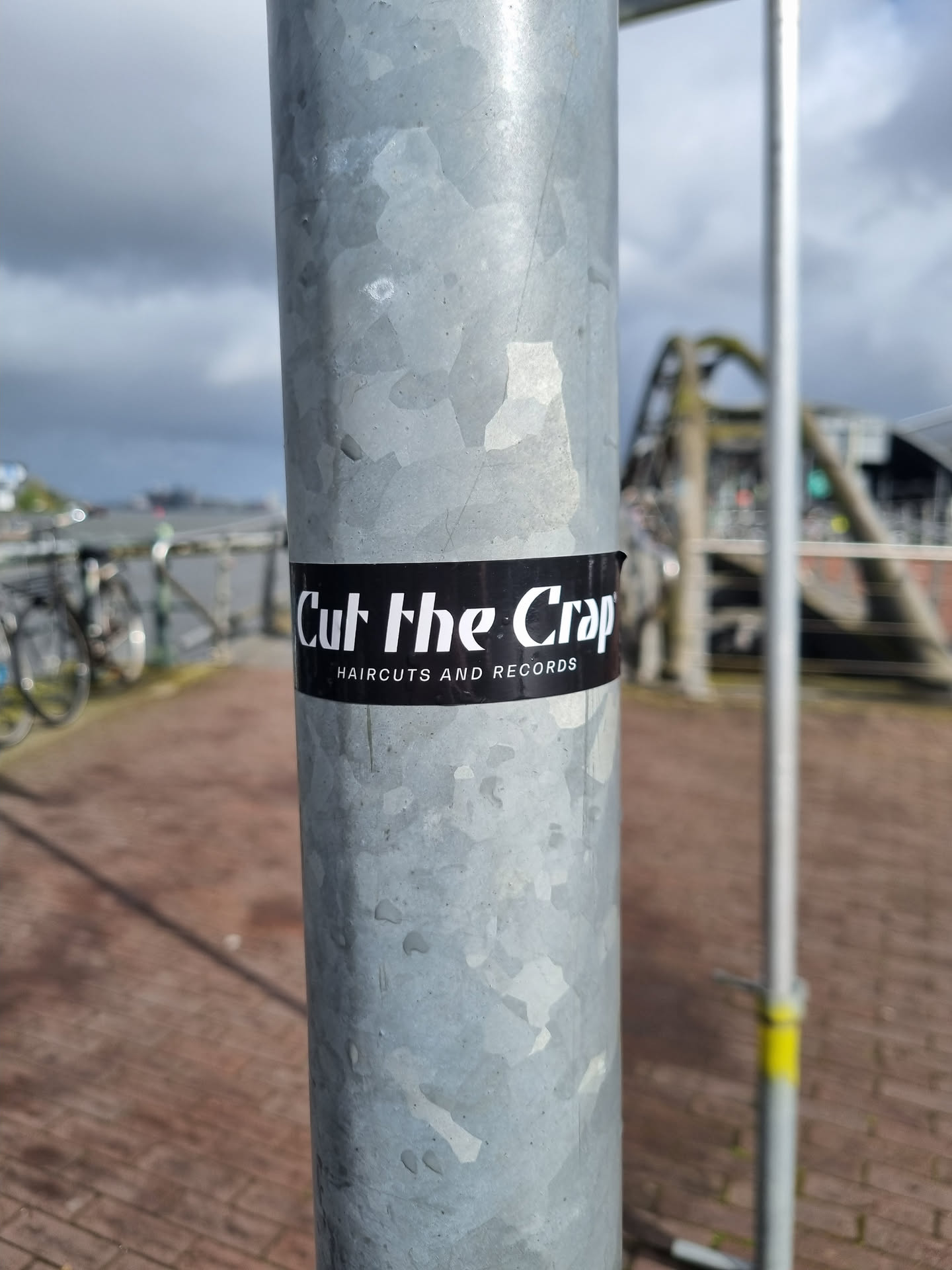 A black and white sticker on a metal pole, advertising a business called "Cut the Crap" which offers haircuts and records.