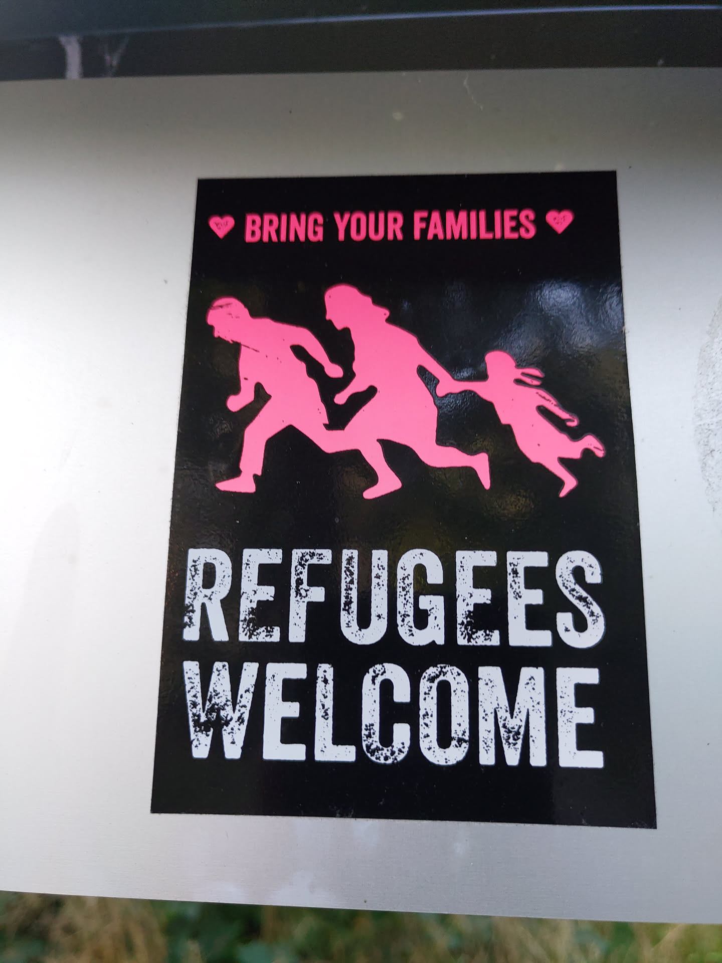 A black and pink sticker with a family silhouette and the text "Refugees Welcome" and "Bring Your Families".