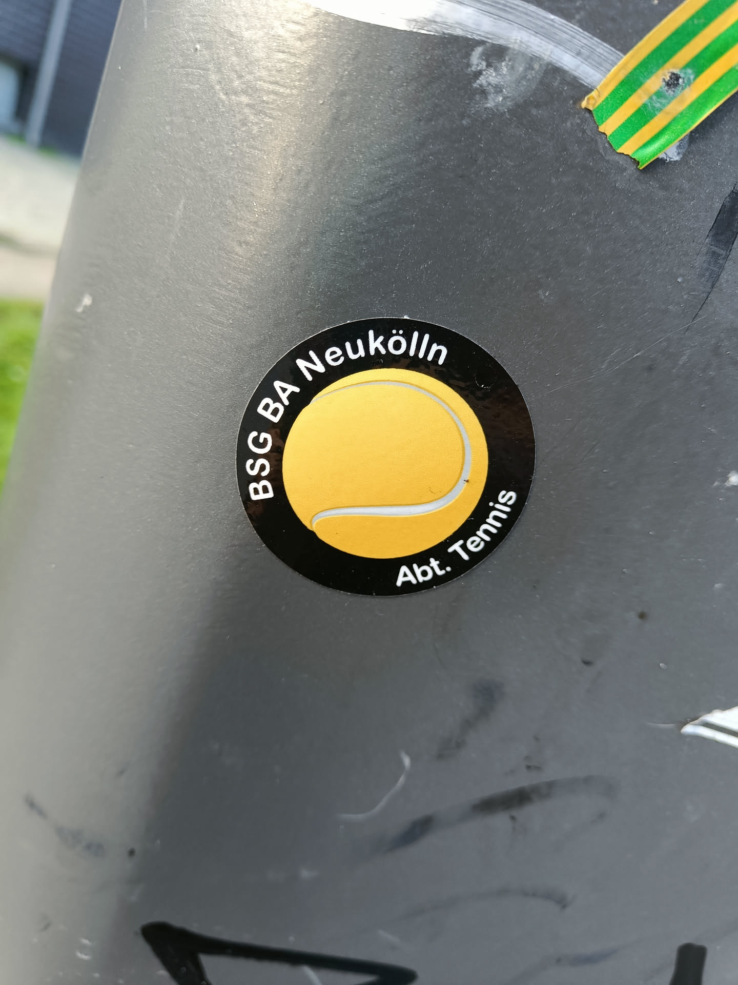 A black and yellow circular sticker featuring a tennis ball graphic and the text 'BSG BA Neukölln Abt. Tennis'.