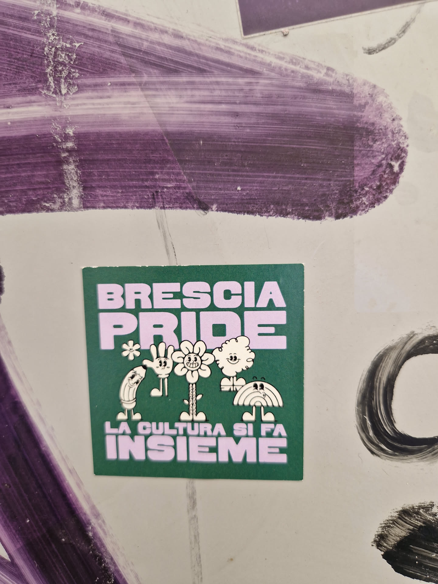 Green sticker with the text Brescia Pride and the phrase La cultura si fa insieme in purple. It features a line of cute cartoon characters.