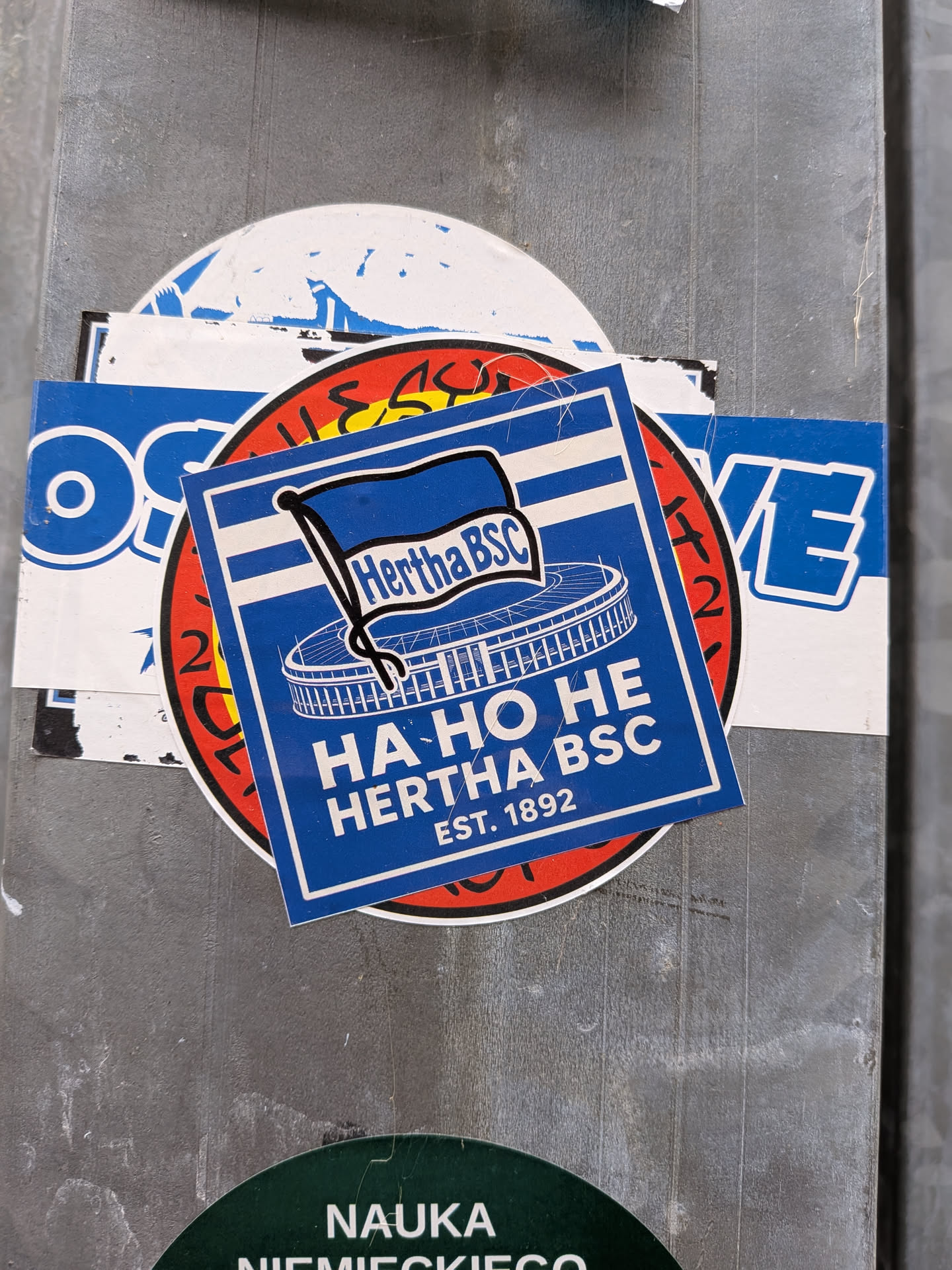 A square blue and white sticker representing the German football club Hertha BSC. It features the team's official waving flag emblem positioned above a stylized white line drawing of the Olympiastadion Berlin. Below the stadium illustration, bold white text reads 'HA HO HE HERTHA BSC EST. 1892'. The sticker is framed with a thin white interior border against a solid blue background.