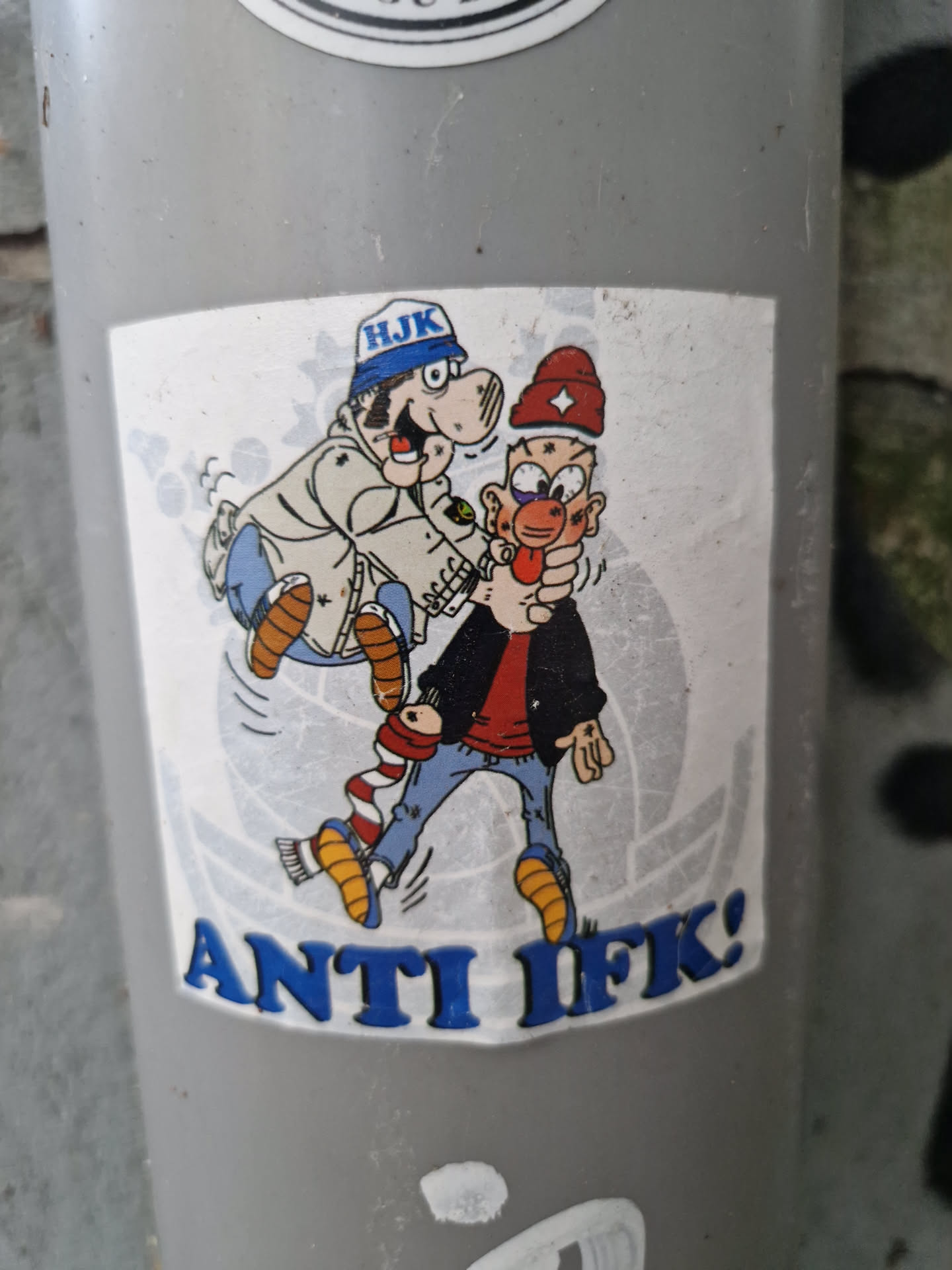 A sticker featuring a cartoon illustration of two characters, one appearing to be a policeman apprehending another. The text "ANTI IFK!" is prominently displayed at the bottom. The style of the cartoon is reminiscent of classic comic strips.