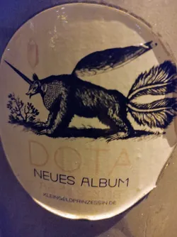 Round sticker featuring a fantastical creature, a mix between an anteater and a unicorn, with wings and a long tail. The text on the sticker says "DOTA NEUES ALBUM" and "KLEINGELOPRINZESSIN.DE".