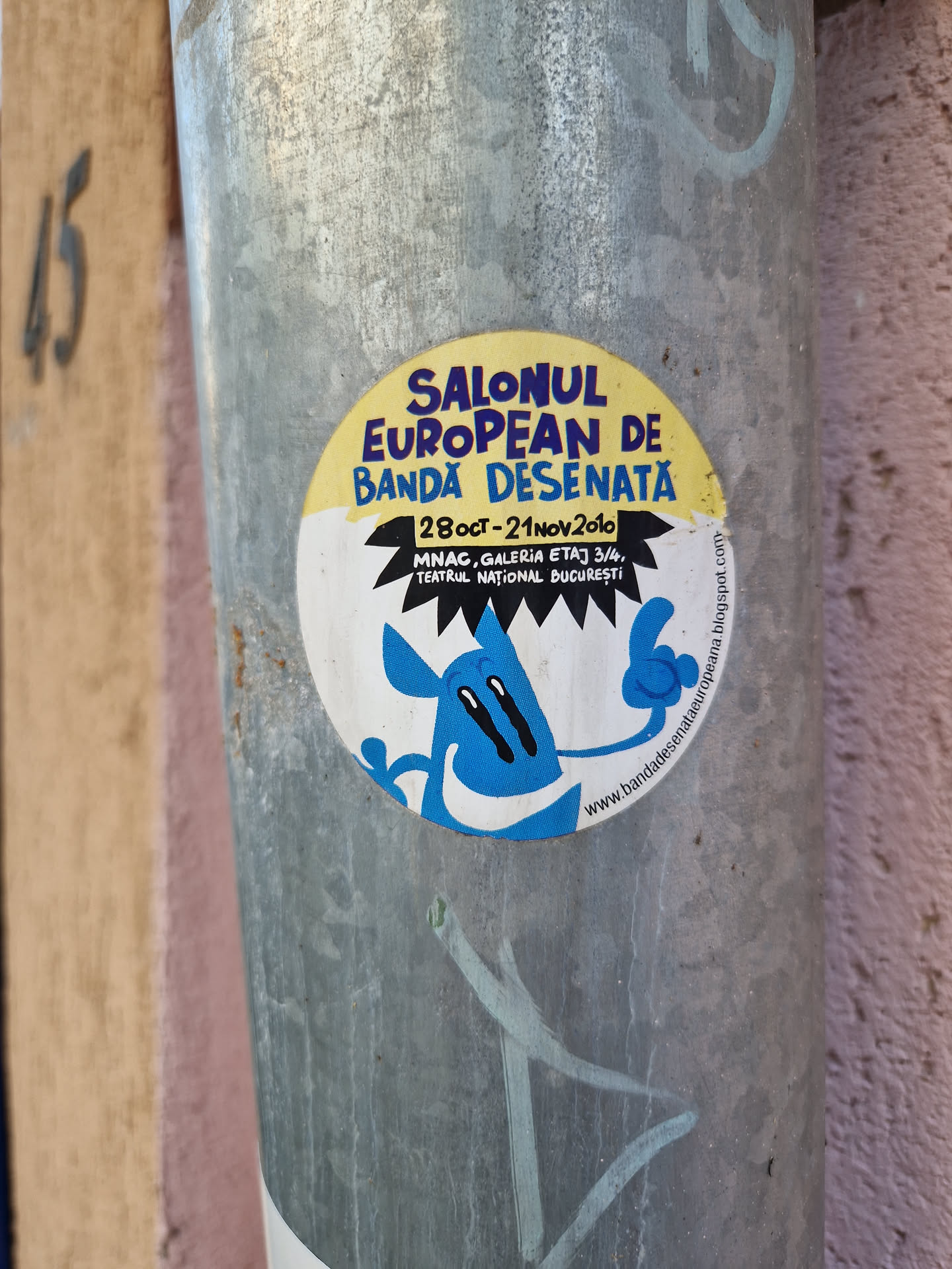 A sticker advertising the European Comics Festival, held in Bucharest from October 28th to November 21st, 2010.  The sticker features a cartoon character and the festival's details, including the location at MNAC, Galeria Etaj 3/4, Teatrul National Bucuresti. A website address is also visible.