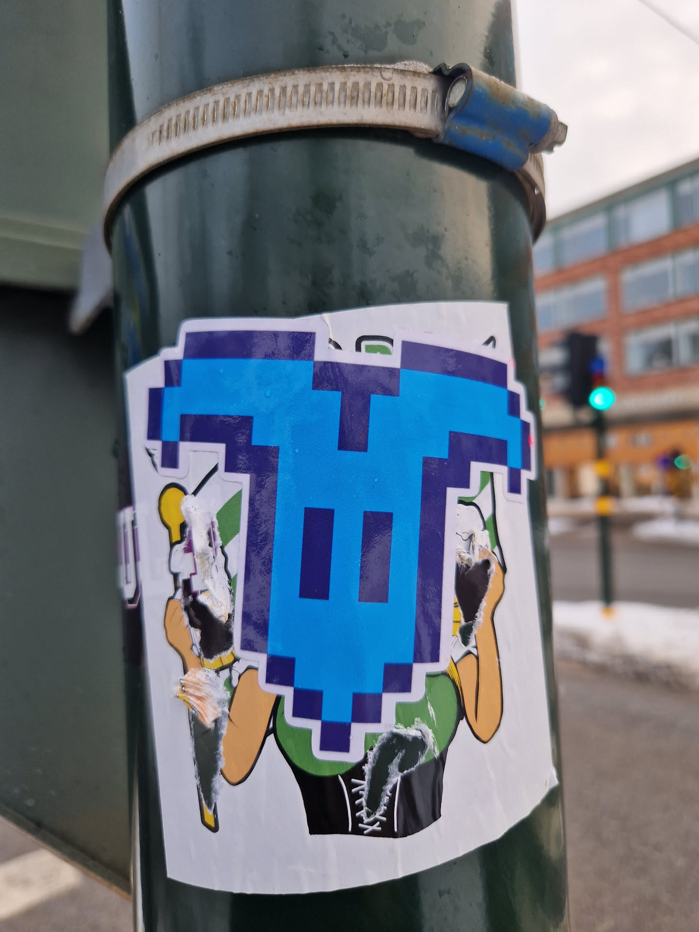 A sticker featuring a pixel art ghost design. The ghost is light blue with dark blue outlines, and is superimposed on an illustration of a woman in a green dress and corset. The sticker is affixed to a green pole.