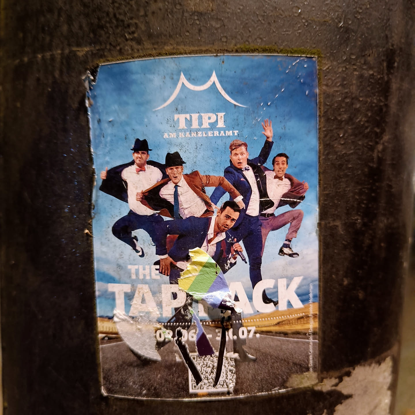 A sticker advertising The TapBack show at Tipi am Kanzleramt.  The sticker features a vibrant image of five performers in mid-dance pose. The dates 08.06 - 31.07 are visible, suggesting a performance run. A QR code is partially visible at the bottom.