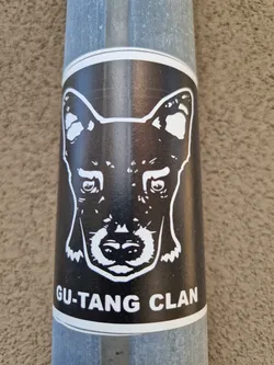 A black and white sticker with a dog's face and the text 'GU.TANG CLAN'. The sticker is on a metal pole.