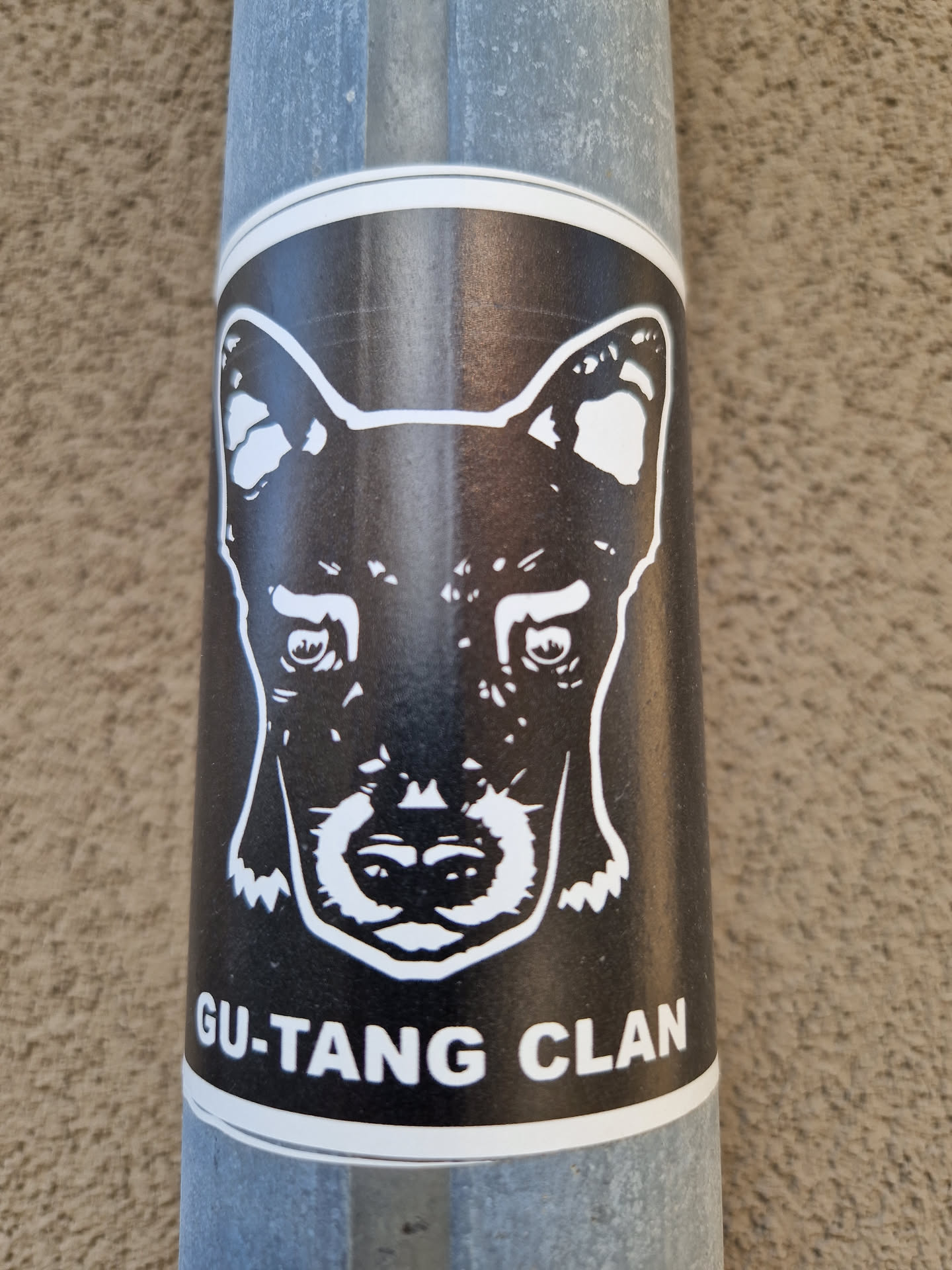 A black and white sticker with a dog's face and the text 'GU.TANG CLAN'. The sticker is on a metal pole.