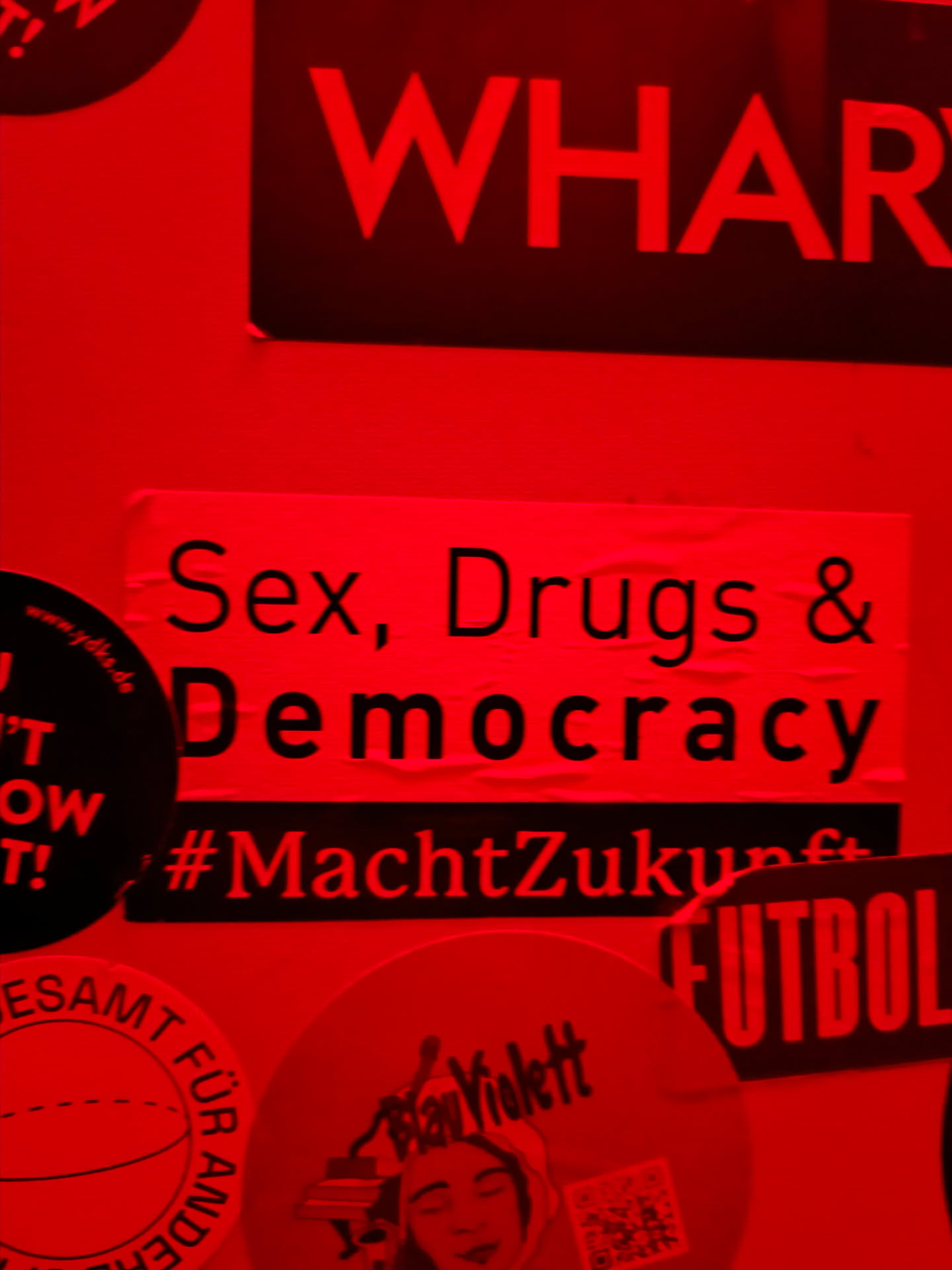 A red sticker with the text "Sex, Drugs & Democracy" and the hashtag #MachtZukunft. The sticker is affixed to a surface with other stickers.
