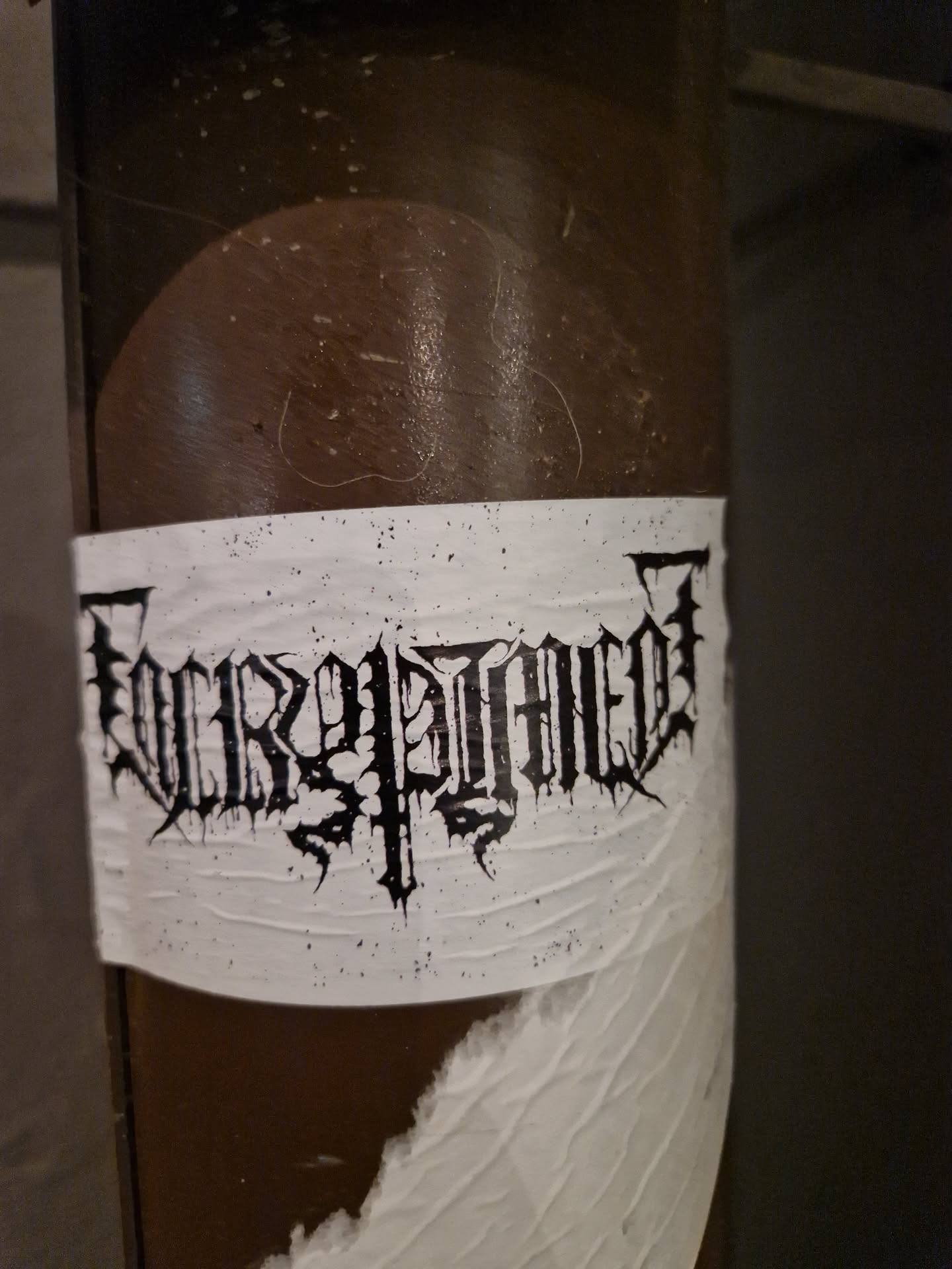 Black and white sticker with the word "Encrypted" written in a stylized font. The sticker is affixed to a brown cylindrical object.  Some of the sticker is peeling at the bottom.