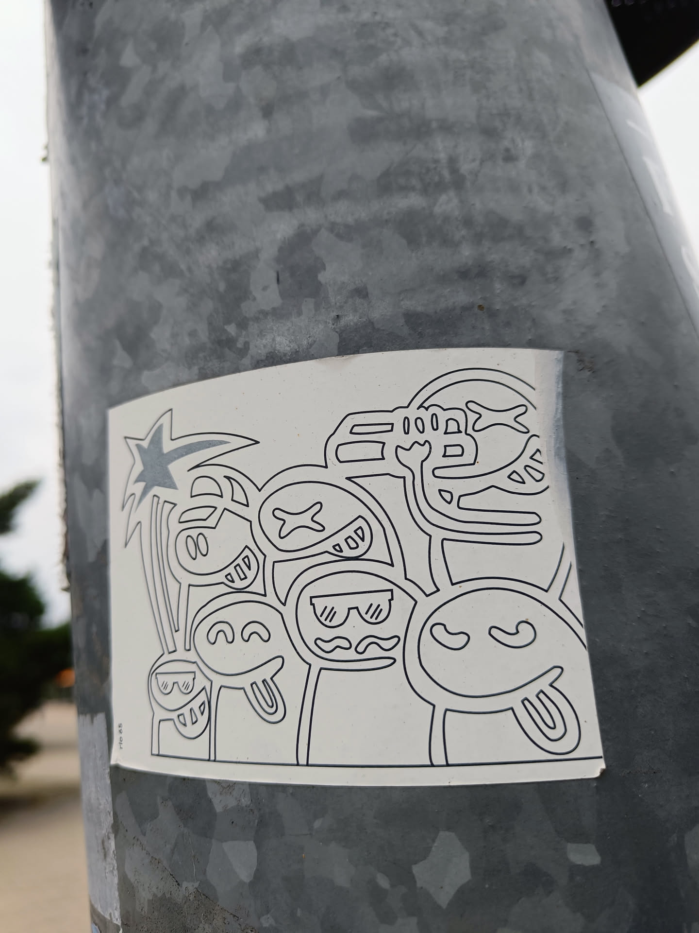 A monochrome sticker featuring a collection of cute, quirky characters with various expressions.  They appear to be enjoying a beach scene with a palm tree. The art style is simple line drawings with some added details.