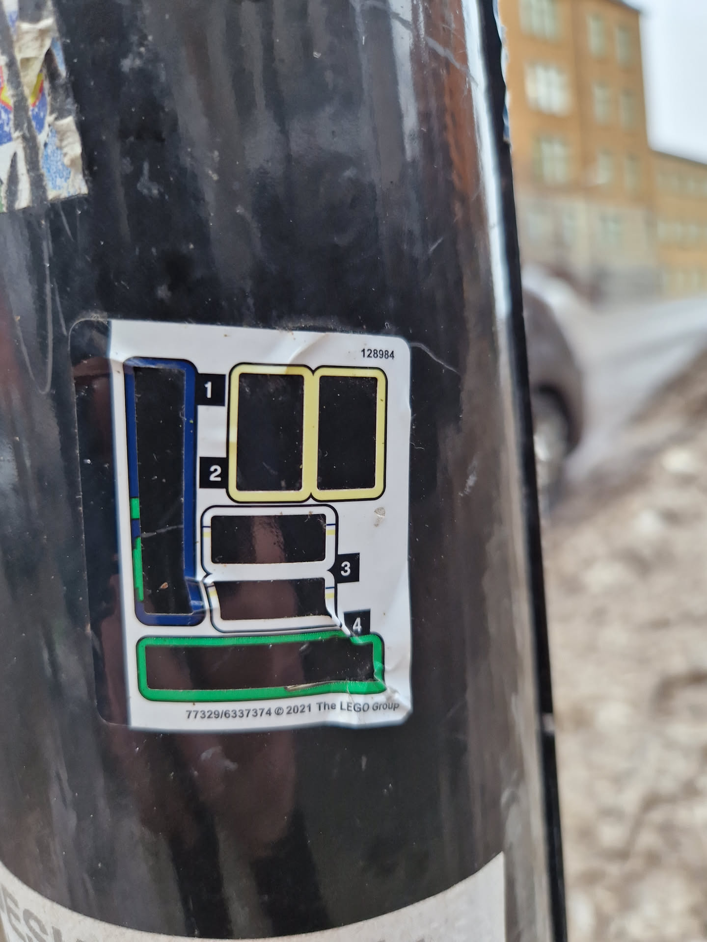 A sticker featuring a diagram, likely showing a map or instructions, with numbers 1-4 indicating different sections.  The text at the bottom includes a number sequence and copyright information for The LEGO Group in 2021. The sticker is affixed to what appears to be a dark-colored pole or post.