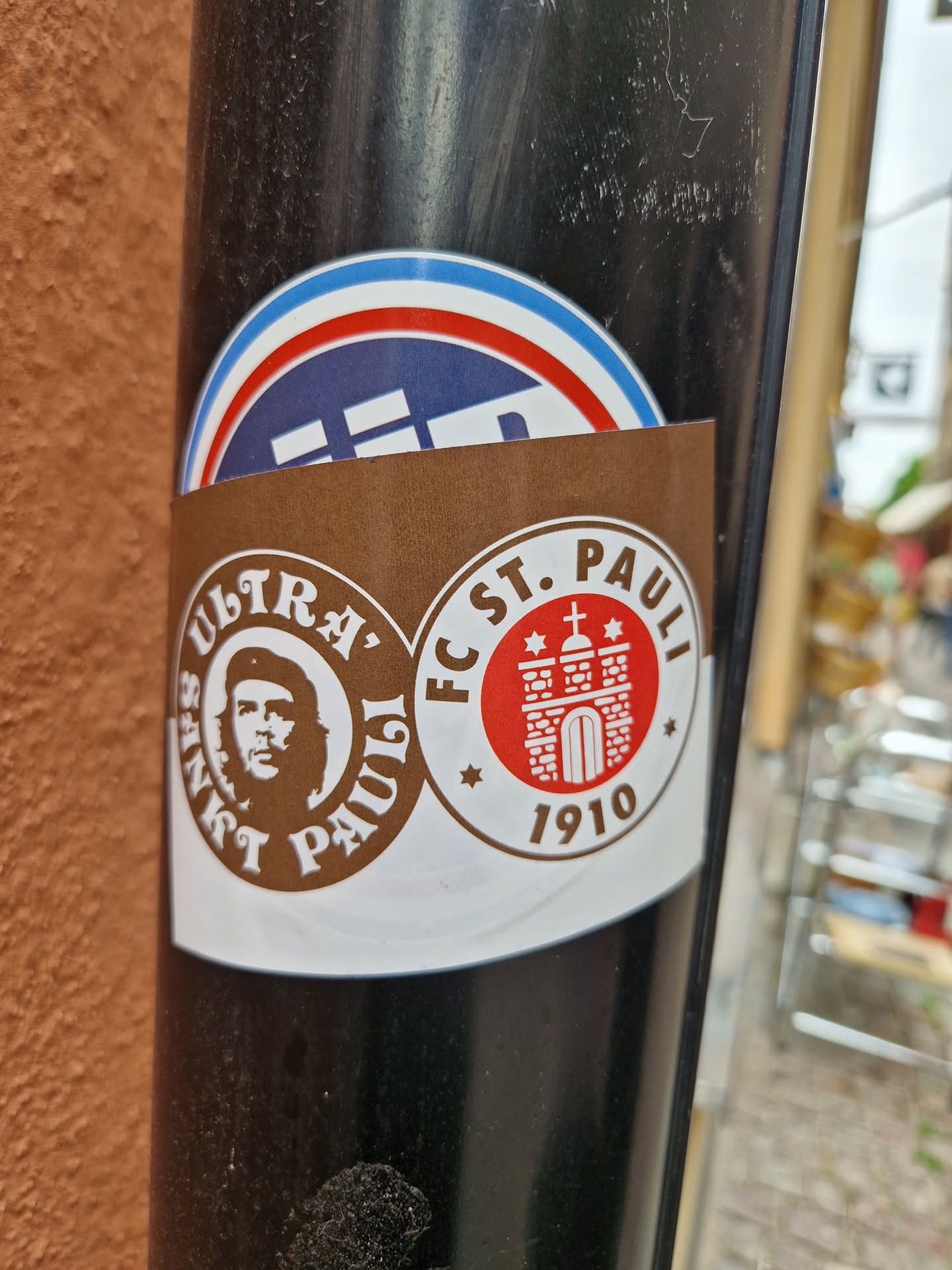 A brown sticker with two circular designs. One features Che Guevara's portrait with the text "Ultra Sankt Pauli" and the other shows the FC St. Pauli logo with the year 1910.