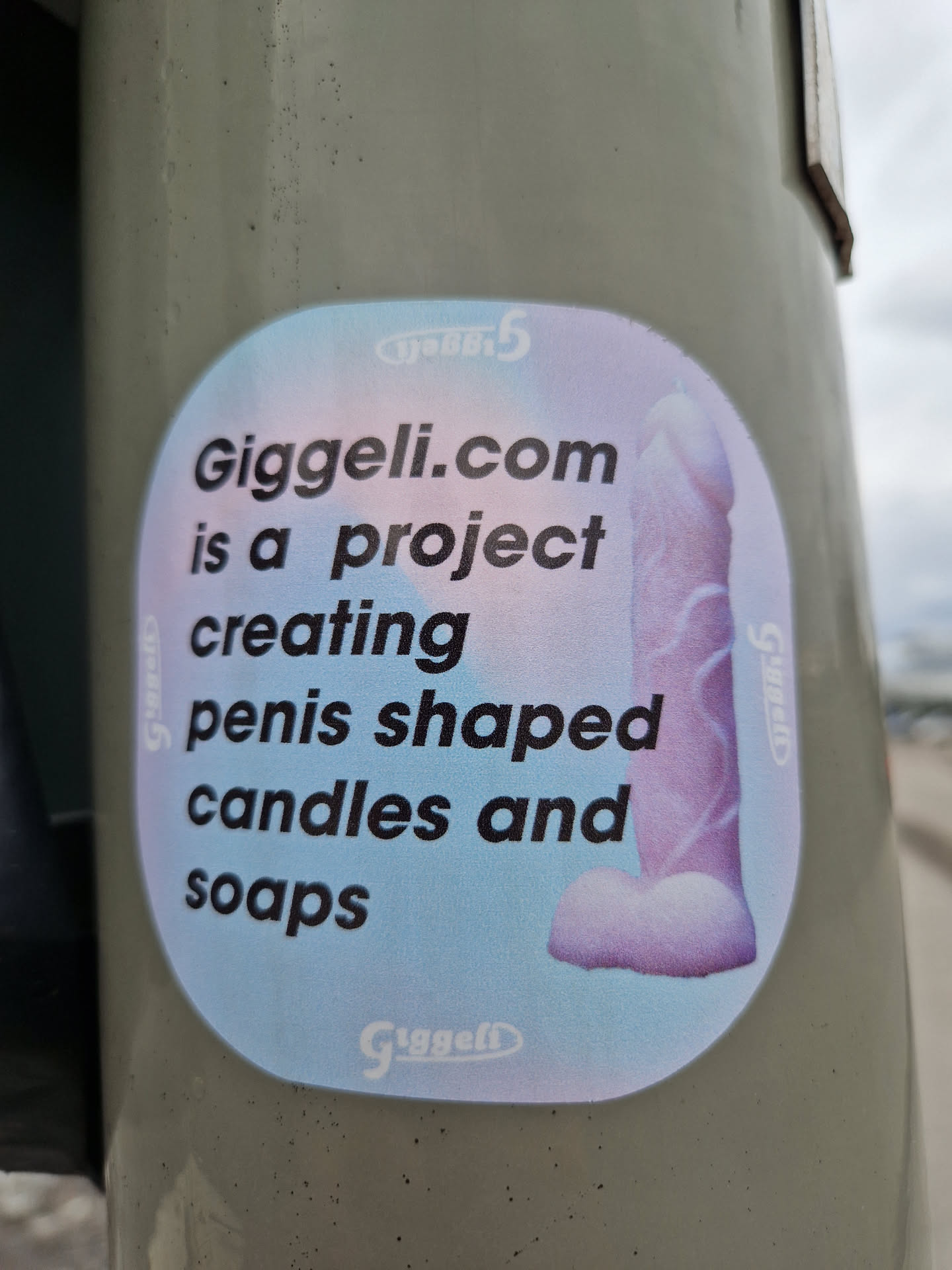 A sticker advertising Giggeli.com, a project that creates penis-shaped candles and soaps. The sticker features an illustration of a penis-shaped candle or soap.